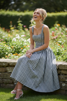 Blonde model seated on garden bench laughing wearing black white gingham fit and flare midi dress with skirt fanned out