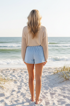 Classic stripe high waist denim shorts back view styled with beige knit sweater on sandy beach, summer outfit inspo
