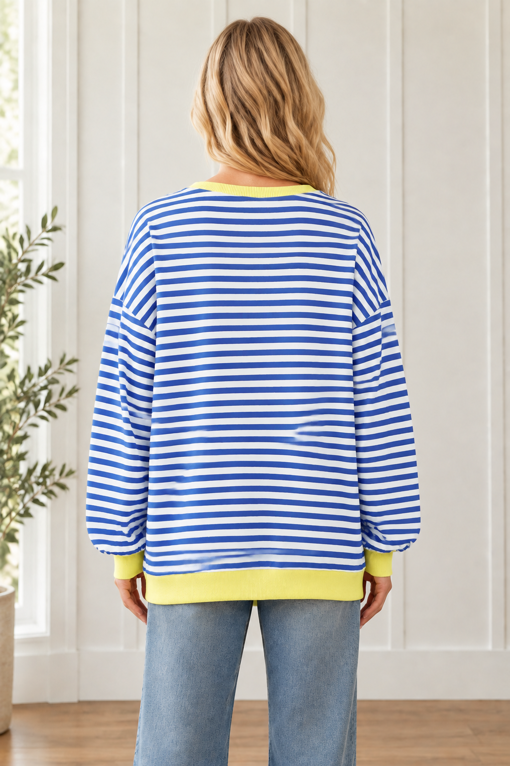 Back view of oversized blue and white striped pullover showing long sleeves and a yellow ribbed hem.