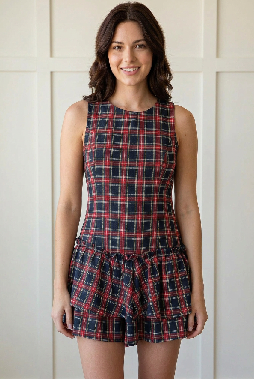 Relaxed front view of the dark tartan plaid romper showing the sleeveless round neck, fitted bodice, and flared layered ruffle shorts.