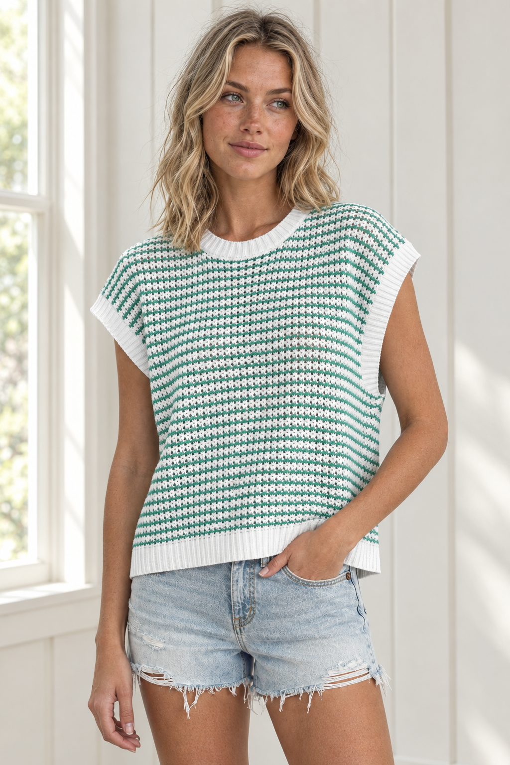 Angled view of green and white striped knit tank top with ribbed neckline and armhole trim, styled with denim shorts