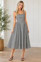 Angled view of black and white gingham square neck dress with wide straps and midi hem