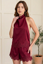 Angled view of a burgundy satin halter top and relaxed shorts, highlighting the sleeveless cut and eyelash lace hems.