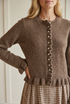 Close-up of the brown cardigan's textured knit, ribbed crew neckline, pale buttons, wavy ruffle placket, and ruffled hem.