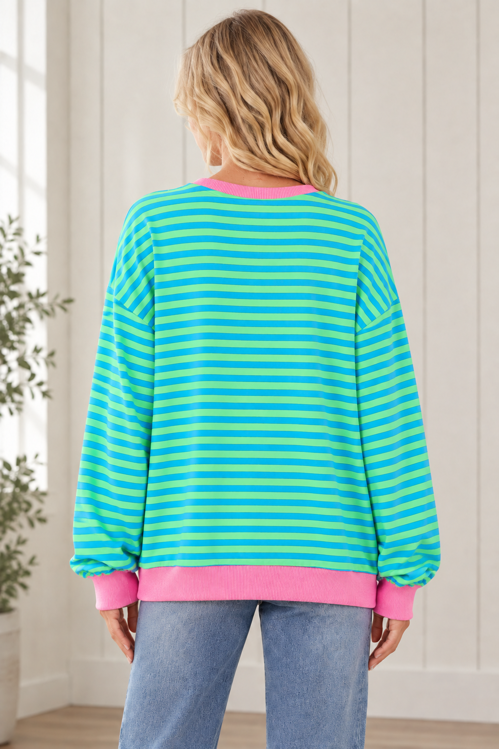 Back view of oversized blue and green striped pullover showing long sleeves and a pink ribbed hem.