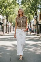Blonde model wearing white ruffled hem wide-leg jeans and leopard knit top, walking down a sunny tree-lined street, hands in pockets, full body lifestyle shot