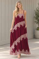 Walking view of flowy burgundy maxi dress with contrast floral lace bands and lace hem