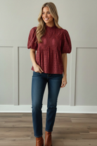 Close-up detail of cranberry eyelet blouse featuring ruffled mock neckline, allover eyelet fabric texture, and ornate tone-on-tone crochet medallion embroidery on bodice