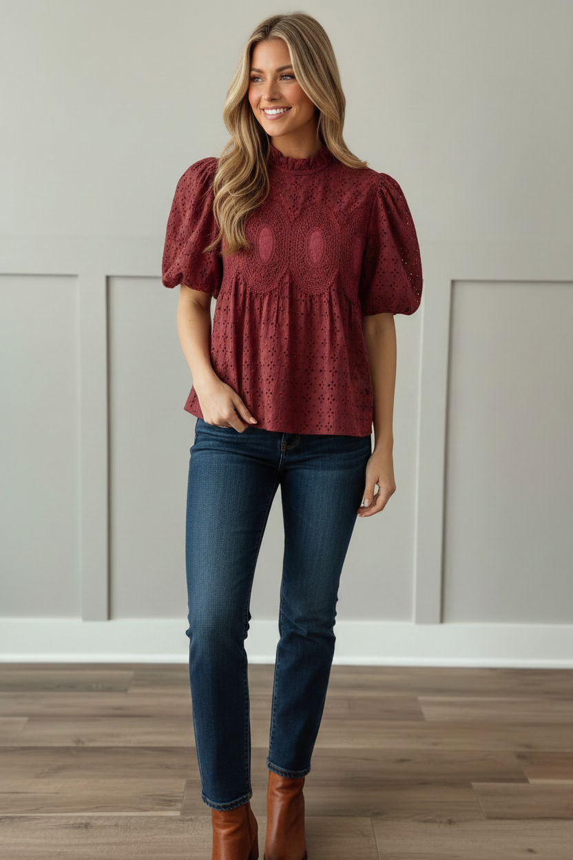 Close-up detail of cranberry eyelet blouse featuring ruffled mock neckline, allover eyelet fabric texture, and ornate tone-on-tone crochet medallion embroidery on bodice