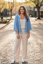 Full body front view of brunette woman outdoors wearing blue stripe boxy knit cardigan open over cream linen tank top with wide-leg linen pants and white sneakers