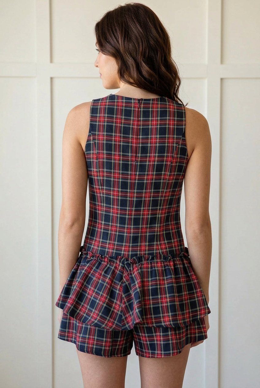 Back view of the sleeveless tartan plaid romper showing the fitted bodice, low gathered waist, and layered ruffles over shorts.