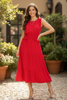 Cherry red smocked waist tiered midi dress full length front view — brunette model hand on hip garden patio gold strappy heels