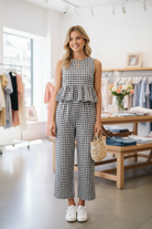 Blonde model standing in boutique wearing black white gingham ruffle back peplum top and wide-leg trouser set holding woven bag