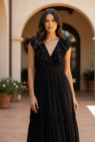Close-up three-quarter shot of brunette model in black ruffle maxi dress highlighting V-neckline ruffle bust detail and smocked waist