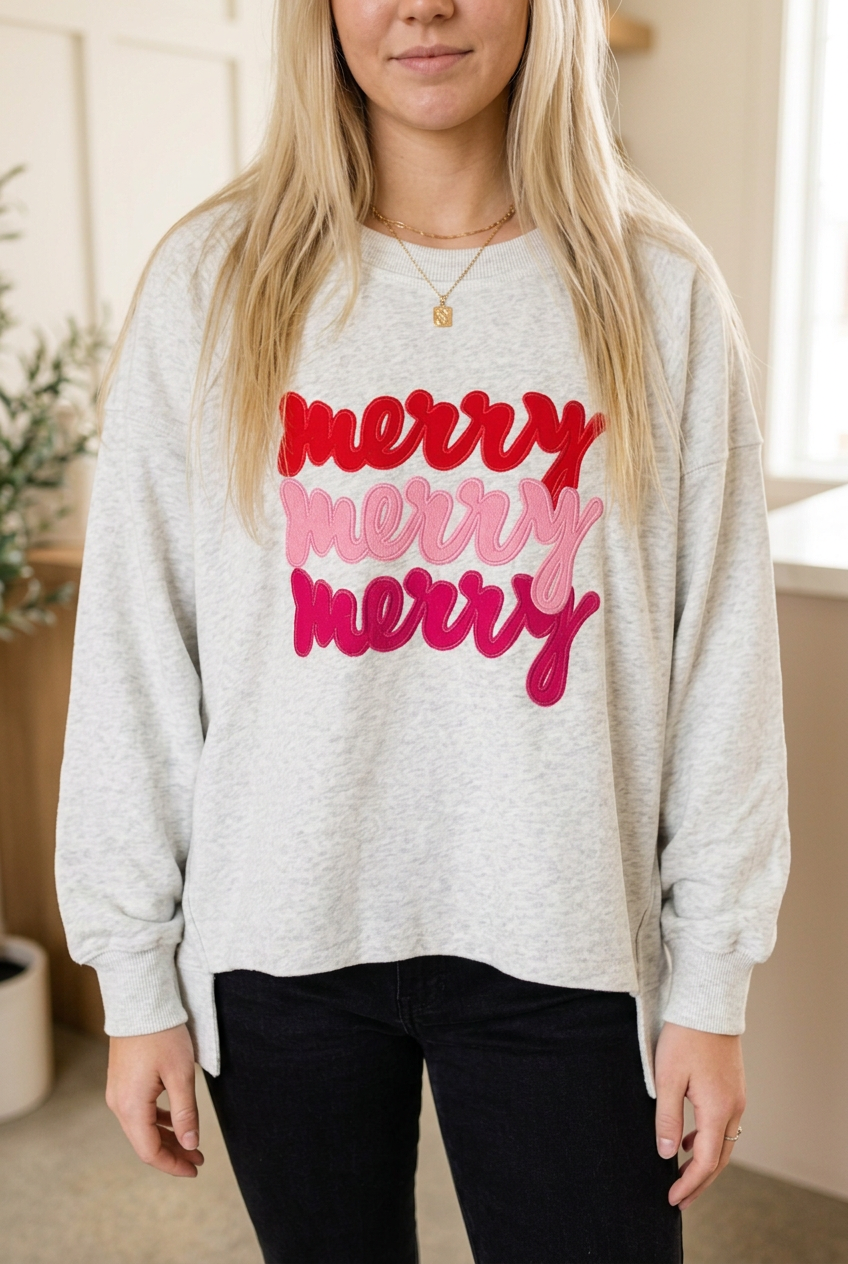 Close-up of light grey Merry Christmas sweatshirt showing red, light pink and deep pink script, round neckline and ribbed cuffs.