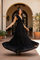 Brunette model twirling in long black ruffle tiered maxi dress outdoors, flowing skirt showing full tiered length in warm natural light