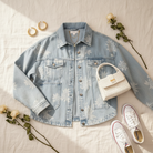 BiBi floral print washed denim jacket styled flat lay, light wash denim with tonal white rose print spread open showing silver snap buttons and large patch pockets, styled with gold jewelry, white sneakers, and dried white roses
