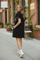 Umgee black LUXEKNIT butterfly sleeve mini dress walking lifestyle shot looking back over shoulder, crochet trim sleeve detail, A-line silhouette, outdoor urban setting