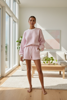 Pink and white gingham cozy chic women's lounge set featuring a plush crewneck sweatshirt and drawstring shorts with pockets in lifestyle setting