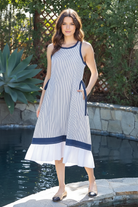 Brunette model wearing navy and white striped contrast hem maxi dress with white ruffle hem, front-facing poolside lifestyle shot