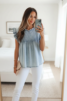 Light blue denim blouse with flutter sleeves, ruffle neckline, and relaxed babydoll fit