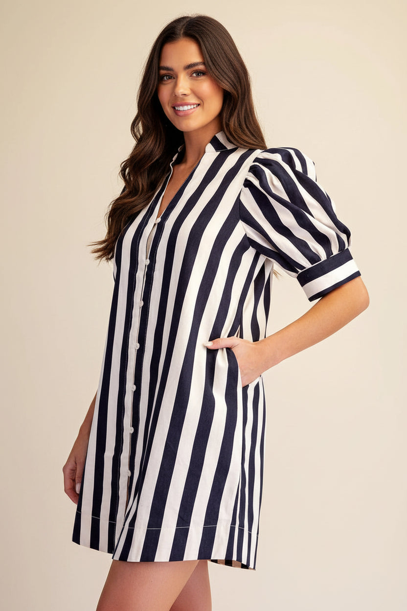 A woman modeling a short puff-sleeve shirt dress with vertical navy and white stripes, set against a plain beige studio background.