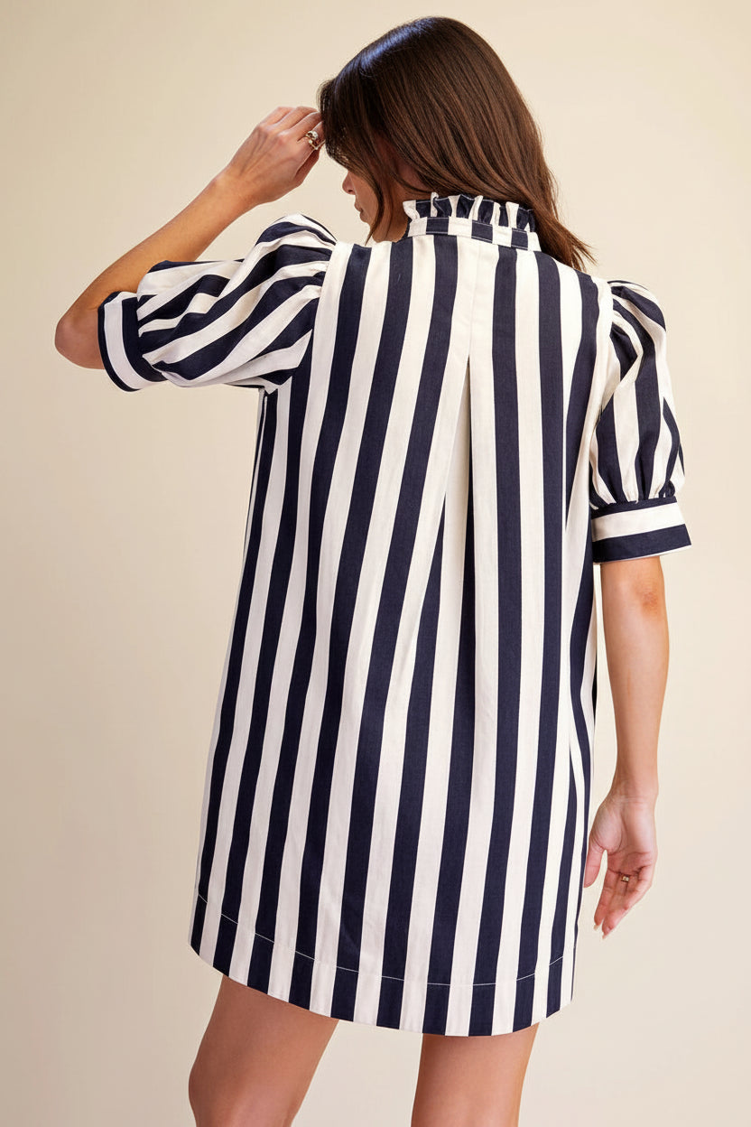 A woman shown from the back wearing a short puff-sleeve shirt dress with bold vertical navy and white stripes, set against a plain beige studio background.