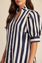 A close-up of a woman wearing a navy and white vertically striped dress with puff sleeves and a button-front collar.