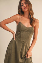 Woman wearing an olive suede bustier midi dress with adjustable straps and a flared skirt — trendy boutique fall outfit.