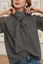 Umgee black polka dot tie neck long sleeve blouse with oversized balloon sleeves and self-tie bow, styled with wide-leg dark wash jeans and tan block heels, boutique women's top at Thread Bar Boutique