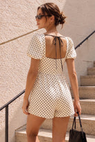 Woman wearing a polka dot romper standing on steps with a neutral wall background
