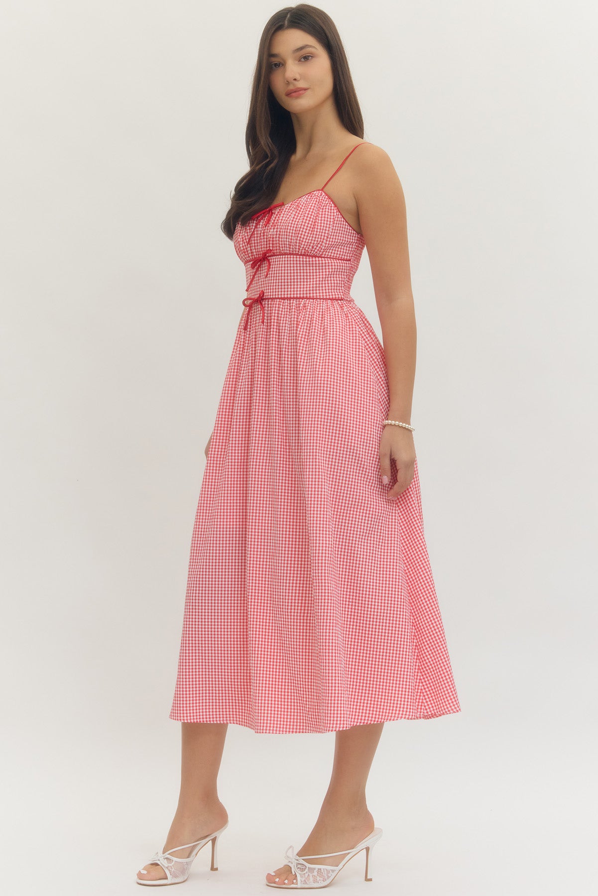 Model wearing a sweetheart gingham maxi dress with adjustable straps, bow details, smocked back, and side pockets in a romantic gingham print, perfect for Valentine’s Day and spring occasions.