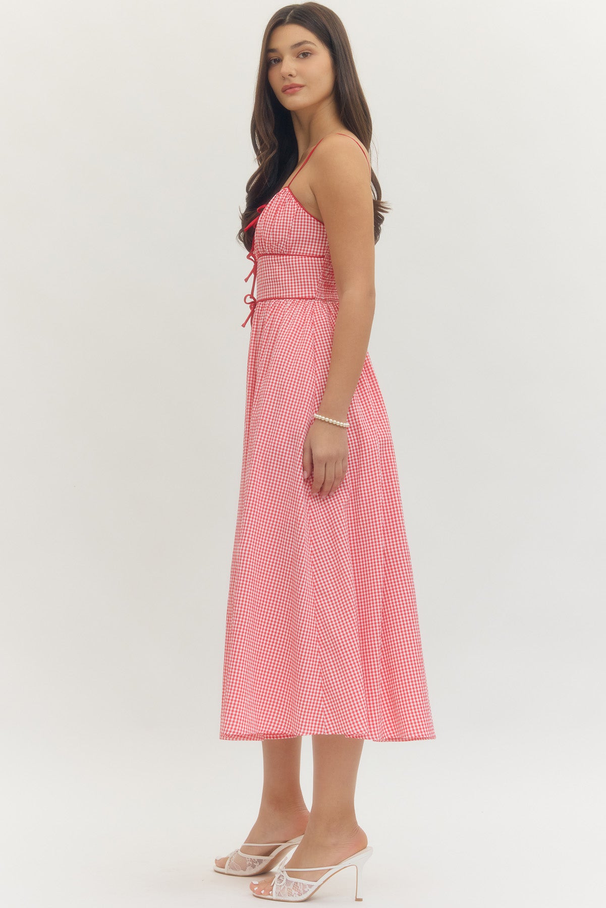 Model wearing a sweetheart gingham maxi dress with adjustable straps, bow details, smocked back, and side pockets in a romantic gingham print, perfect for Valentine’s Day and spring occasions.