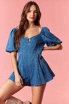 Woman wearing a game day denim romper with bubble sleeves and pleated detail with tie back