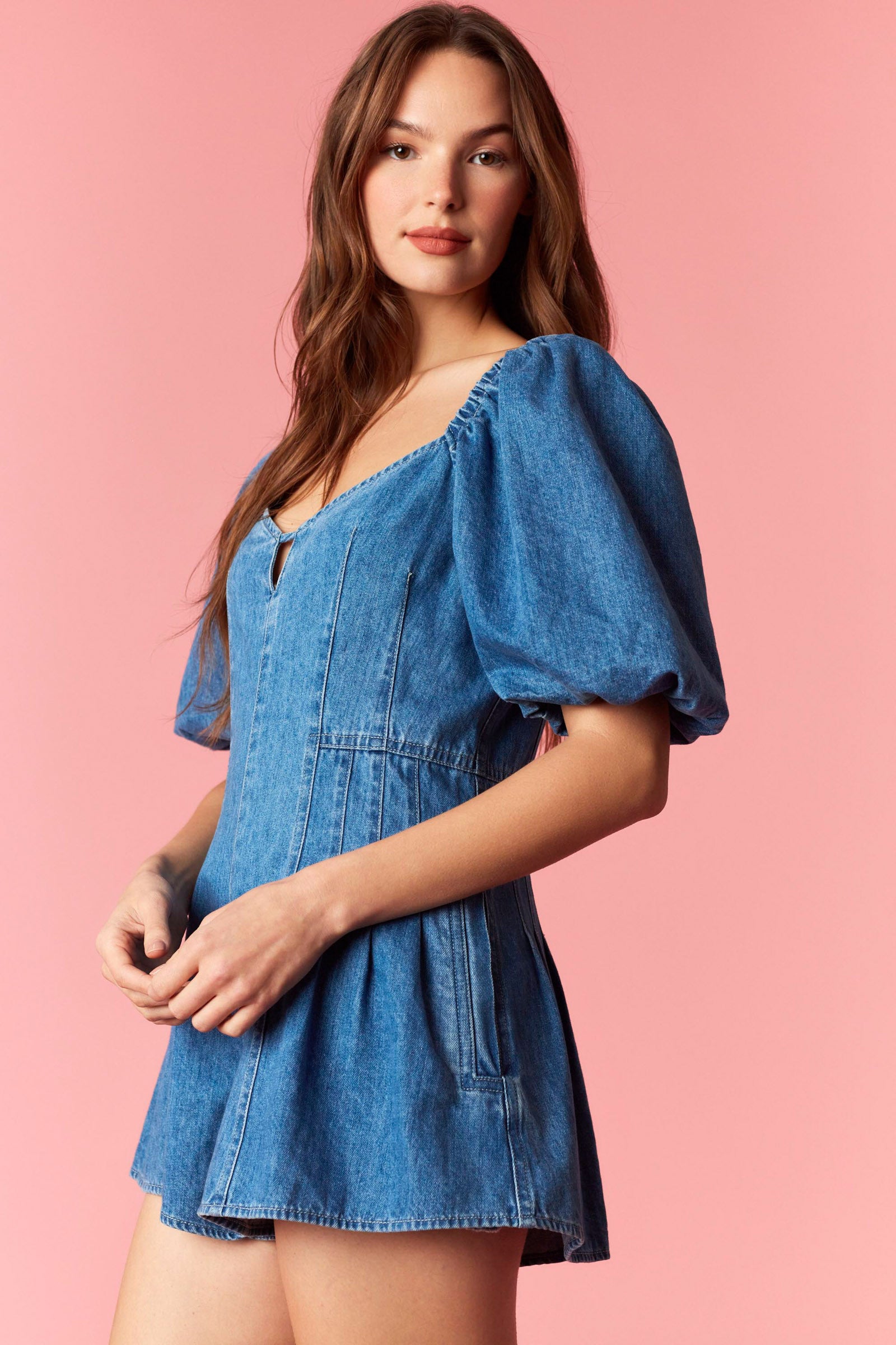 Woman wearing a game day denim romper with bubble sleeves and pleated detail with tie back