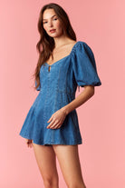 Woman wearing a game day denim romper with bubble sleeves and pleated detail with tie back