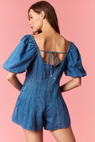 Woman wearing a game day denim romper with bubble sleeves and pleated detail with tie back