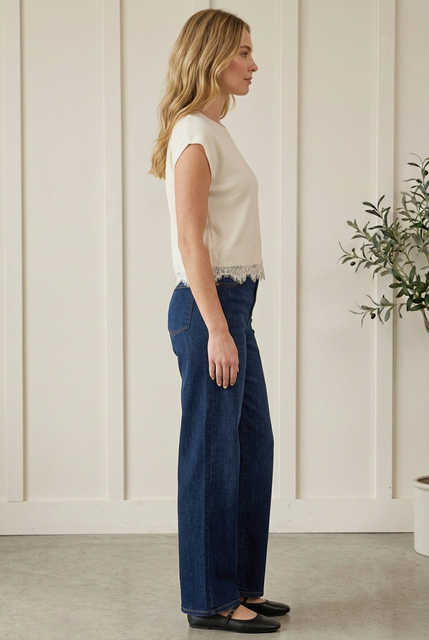 Side view of cream sweater top showing cap sleeves, an easy silhouette and lace trim hem, paired with dark jeans.