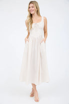 Sleeveless striped dress in a neutral taupe and white vertical pattern. This A-line summer dress features a structured corset waist dress bodice with a decorative tie-front midi neckline and a voluminous calf-length skirt with functional side pockets