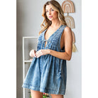 Woman wearing a stylish sleeveless denim romper with deep V-neckline, front pleats, and tie detail at the bust; perfect trendy summer outfit for women from a boutique collection.