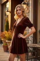 Blonde college-age model in chocolate brown velvet A-line mini dress, 3/4 angle outdoor lifestyle shot, lace neckline detail visible