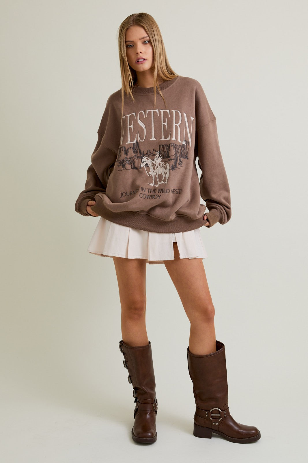 Woman wearing a mocha oversized crewneck sweatshirt with “Western” embroidery and a cowboy graphic