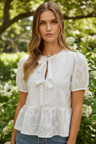 Romantic white eyelet blouse from Thread Bar Boutique with short sleeves and front bow tie detail for spring and summer outfits.