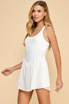 White athletic dress with crisscross racerback straps, a corset-style waist, and built-in shorts with pockets. Designed for movement, workouts, and everyday sporty-chic style.